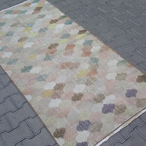 May include: A rectangular rug with a repeating pattern of colorful, cloud-like shapes in pastel shades of pink, yellow, blue, and brown. The rug has a beige background and a fringed edge. The rug is placed on a gray brick surface.