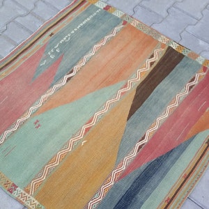 May include: A colorful, geometric patterned rug with a mix of red, orange, blue, green, and brown tones. The rug has a fringed border.