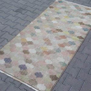 May include: Rectangular rug with a floral pattern in pastel colors. The rug features a cream-colored background with scattered flower-like shapes in shades of pink, blue, yellow, and brown. The rug is placed on a gray brick surface.