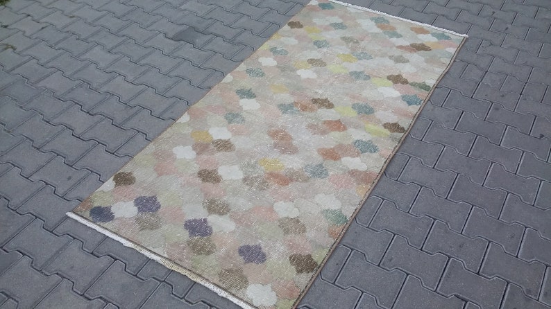 May include: Rectangular rug with a floral pattern in pastel colors. The rug features a cream-colored background with scattered flower-like shapes in shades of pink, blue, yellow, and brown. The rug is placed on a gray brick surface.