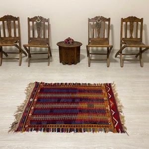 May include: Four wooden folding chairs with carved details surround a small wooden table with a colorful rug in front of it.