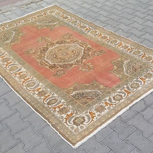 Puede incluir: Alfombra rectangular de estilo vintage con un dise&ntilde;o central de medall&oacute;n en tonos coral, marr&oacute;n y beige. La alfombra presenta un borde ornamentado con patrones florales y geom&eacute;tricos. Se encuentra sobre una superficie de ladrillos grises.