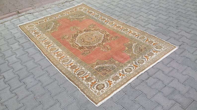 Puede incluir: Alfombra rectangular de estilo vintage con un dise&ntilde;o central de medall&oacute;n en tonos coral, marr&oacute;n y beige. La alfombra presenta un borde ornamentado con patrones florales y geom&eacute;tricos. Se encuentra sobre una superficie de ladrillos grises.