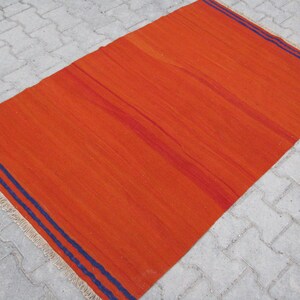 K&ouml;nnte beinhalten: Ein leuchtend orangefarbener Teppich mit zwei dunkelblauen Streifen an den R&auml;ndern. Der Teppich hat einen Fransenrand.