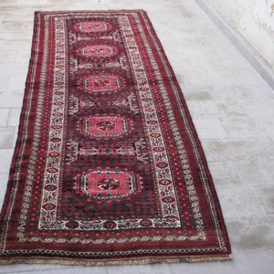 Puede incluir: Una alfombra larga y estrecha de color rojo, negro y blanco con un diseño persa tradicional. La alfombra tiene flecos en ambos extremos.