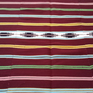May include: A woven fabric with a striped pattern in shades of red, yellow, green, blue, and white. The fabric has a geometric design in the center.