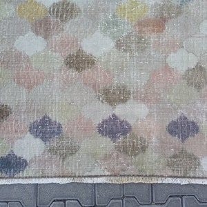 May include: A rectangular rug with a repeating pattern of quatrefoil shapes in muted colors including pink, brown, green, and purple. The rug has a distressed, vintage look with a fringed edge.