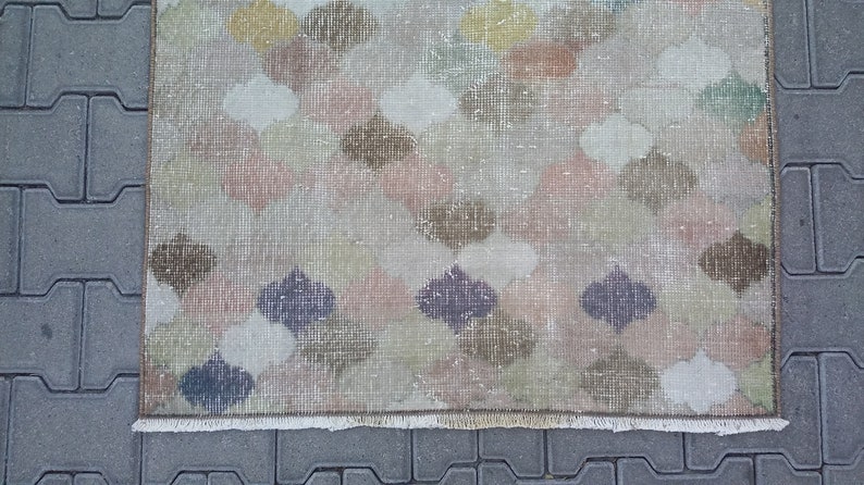 May include: A rectangular rug with a repeating pattern of quatrefoil shapes in muted colors including pink, brown, green, and purple. The rug has a distressed, vintage look with a fringed edge.