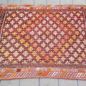 May include: A vintage rug with a geometric pattern in shades of red, orange, and yellow. The rug has a border with a more intricate design.