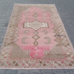 Puede incluir: Una alfombra vintage rosa y beige con un patrón geométrico. La alfombra tiene un aspecto descolorido y está hecha de lana.