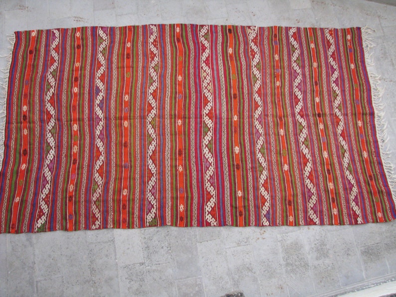 May include: A colorful striped rug with a geometric pattern. The rug is made of wool and has a fringe on the ends.