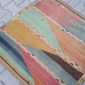 May include: A vintage rug with a geometric pattern in shades of blue, green, orange, and red. The rug has a faded, worn look, giving it a rustic and antique feel.