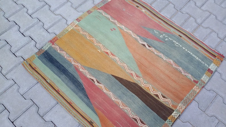 May include: A vintage rug with a geometric pattern in shades of blue, green, orange, and red. The rug has a faded, worn look, giving it a rustic and antique feel.