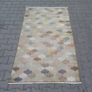 May include: A rectangular rug with a repeating pattern of colorful, stylized floral shapes in shades of pink, blue, yellow, and brown. The rug has a beige background and a fringed edge. The rug is approximately 3 feet wide and 5 feet long.
