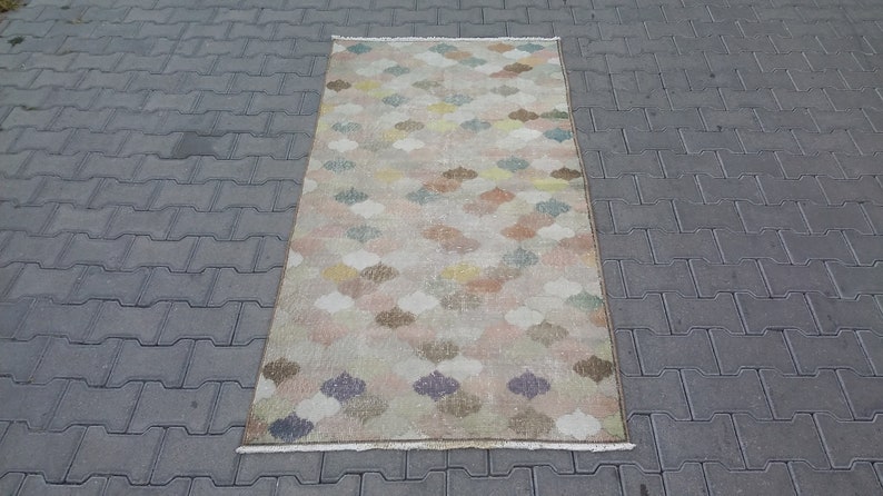 May include: A rectangular rug with a repeating pattern of colorful, stylized floral shapes in shades of pink, blue, yellow, and brown. The rug has a beige background and a fringed edge. The rug is approximately 3 feet wide and 5 feet long.