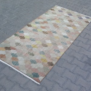 May include: Rectangular rug with a repeating pattern of colorful, cloud-like shapes in pastel shades of pink, yellow, blue, and brown. The rug has a cream-colored border and is placed on a gray, textured surface.