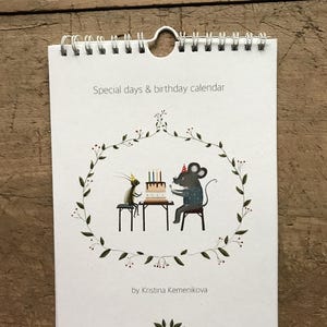 Puede incluir: Calendario encuadernado en espiral con el texto "Special days & birthday calendar". La portada presenta una ilustración de dos ratones en una fiesta de cumpleaños. La obra de arte está rodeada por una corona floral verde. El nombre del artista está en la parte inferior.