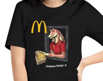 Peut inclure: T-shirt noir avec un M jaune et un personnage de dessin animé en uniforme rouge tenant un sac brun. Le texte "meesa lovin' it" est sous le personnage.