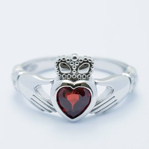 May include: A silver Claddagh ring with a red heart-shaped gemstone and a crown on top.