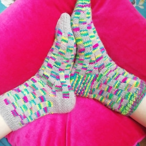 May include: A pair of gray knitted socks with a colorful geometric pattern. The socks are on a pink surface.