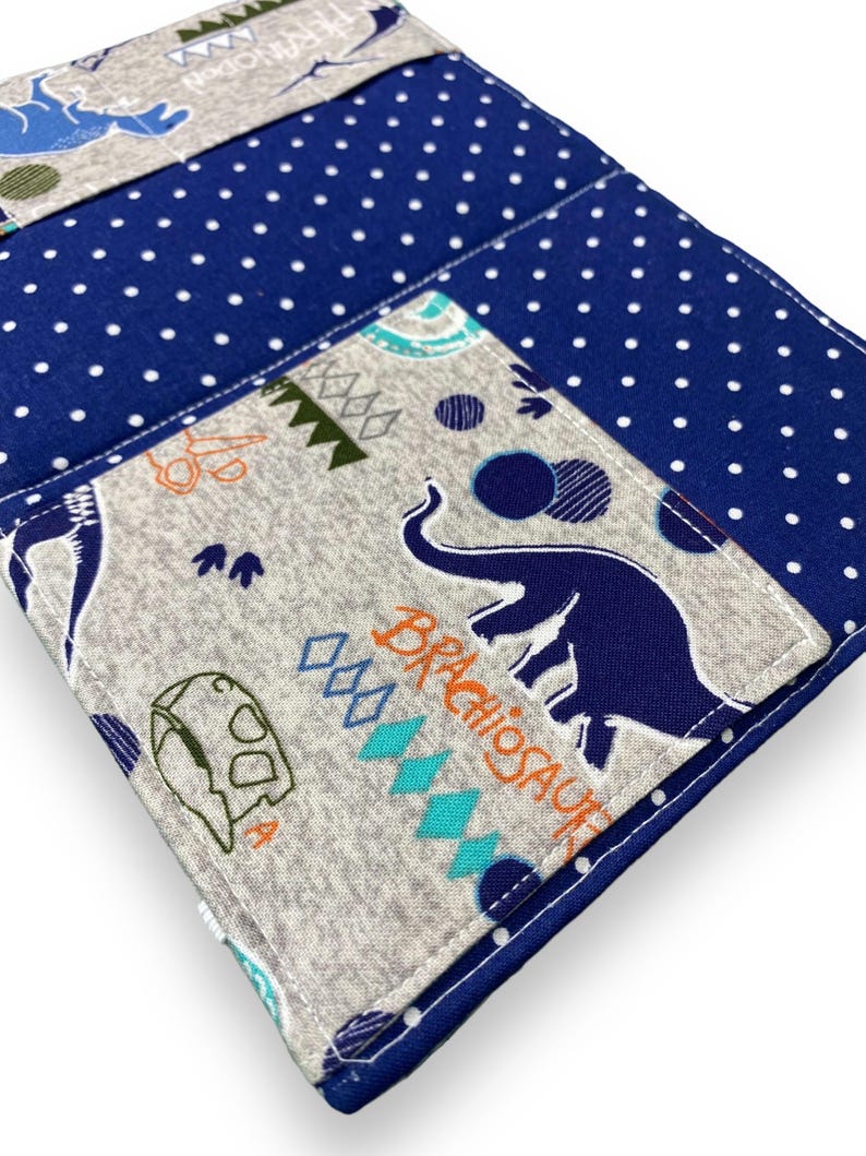 K&ouml;nnte beinhalten: Eine blaue und wei&szlig;e Stoffbrieftasche mit Polka Dots und einer grauen Tasche mit einem blauen Elefanten und dem Wort "Brachiosaurus". Die Brieftasche hat ein Dinosaurier-Thema mit anderen Dinosaurier-Illustrationen.