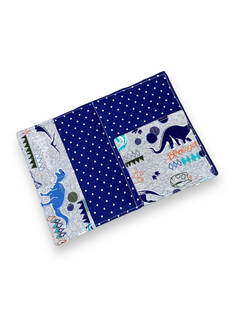 K&ouml;nnte beinhalten: Ein rechteckiger Stoffartikel mit einem Patchwork-Design. Das Design umfasst einen Abschnitt aus marineblauem Stoff mit wei&szlig;en Punkten und Abschnitte aus grauem Stoff mit blauen Dinosaurier-Illustrationen und dem Wort "Brachiosaur".