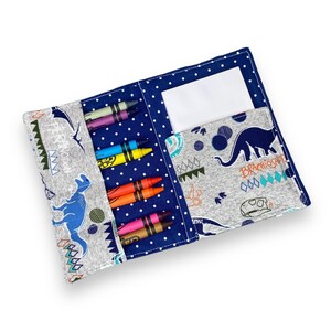 K&ouml;nnte beinhalten: Offenes Stiftetui mit blauem Tupfen- und Dinosaurier-Print-Design. Das Etui ist ge&ouml;ffnet und zeigt mehrere bunte Buntstifte und eine wei&szlig;e Karte. Das Etui ist aus Stoff und hat eine Tasche f&uuml;r die Buntstifte.