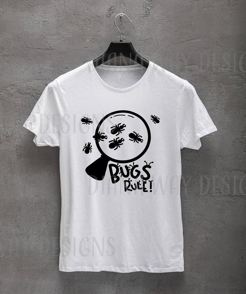 Puede incluir: Camiseta blanca con un dise&ntilde;o negro de una lupa llena de insectos. El texto "BUGS RULE!" est&aacute; debajo. La camiseta est&aacute; colgada en una percha negra sobre un fondo gris.