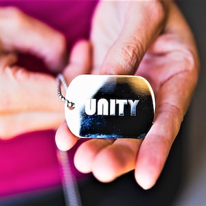 May include: A silver dog tag necklace with the word "UNITY" engraved on it.