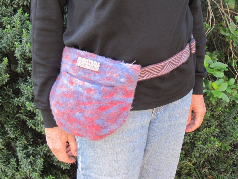 K&ouml;nnte beinhalten: Eine rote, blaue und wei&szlig;e gemusterte Stofftasche, die als G&uuml;rteltasche getragen wird. Die Tasche hat ein silbernes Schild mit dem Text "Studio 33" darauf.
