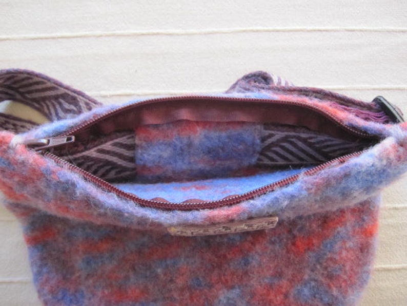 K&ouml;nnte beinhalten: Eine blaue und rote gemusterte Wollschultertasche mit Rei&szlig;verschluss. Die Tasche ist offen und das Innenfutter ist sichtbar.