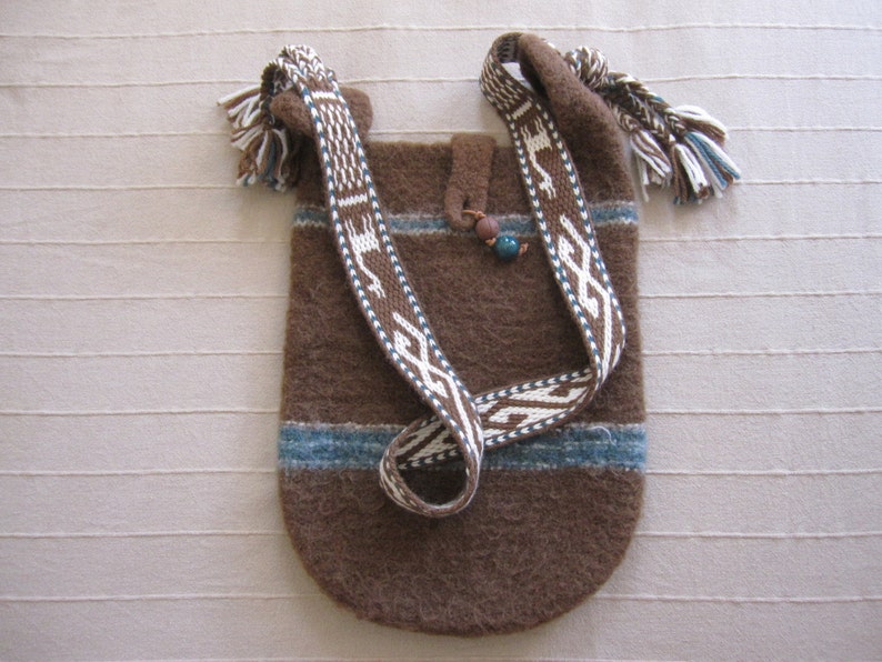 May include: A brown wool bag with a woven strap. The strap has a white and blue geometric pattern. The bag has a blue and white trim.