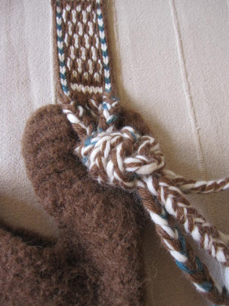 May include: A brown wool pouch with a white and blue braided strap. The strap is tied in a knot at the top of the pouch.
