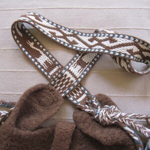 May include: A brown woven strap with white and blue geometric patterns. The strap is tied in a knot and has fringe on the ends.