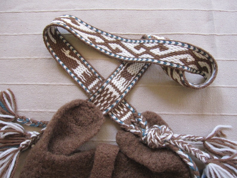 May include: A brown woven strap with white and blue geometric patterns. The strap is tied in a knot and has fringe on the ends.