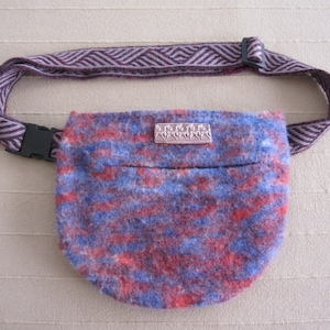 K&ouml;nnte beinhalten: Eine kleine, blaue und rote Stofftasche mit einem lila und wei&szlig;en, gestreiften Riemen. Die Tasche hat ein kleines Metallschild mit dem Wort "ZARA" darauf.