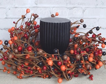 May include: A black pillar candle holder surrounded by a brown berry wreath with red, orange, and black berries.