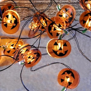 May include: String of lights with orange pumpkin-shaped lights. Each light has a black jack-o'-lantern face.