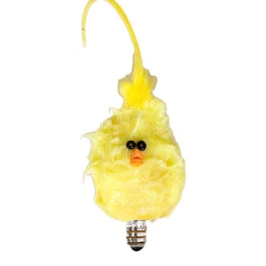 May include: A whimsical, yellow chick-shaped light bulb with black eyes and an orange beak. The bulb has a decorative, feathery appearance and a curved yellow accent extending upwards. The base of the bulb is silver.