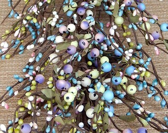 May include: A decorative garland featuring brown wire branches adorned with numerous small, round berries in pastel shades of light blue, lavender, pale yellow, and white, interspersed with small, thin, dark green fabric leaves throughout.