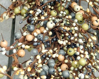 Op de afbeelding: Close-up van een decoratieve slinger met kleine, ronde bessen in crème, grijs, groen en perzik. De bessen zijn bevestigd aan bruine, takachtige stelen, wat een natuurlijke en rustieke uitstraling creëert. Geschikt voor woondecoratie.