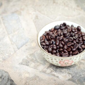 May include: A white ceramic bowl with a floral design filled with dark brown coffee beans.