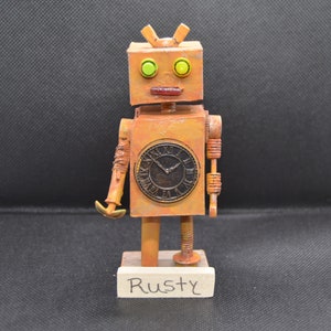 May include: A rusty, orange robot with a clock face and green eyes. The robot is standing on a wooden base with the word "Rusty" written on it.