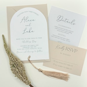 May include: A wedding invitation with a beige background and a white arch. The invitation reads "Alexa and Luka" and includes the wedding date, time, and location. The RSVP card is beige with the text "Kindly RSVP by 20.03.2023".