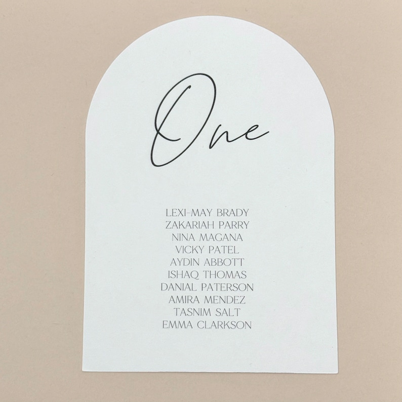 May include: White arch-shaped card with the word "One" written in black cursive. The card lists the names of ten guests: Lexi-May Brady, Zakariah Parry, Nina Magana, Vicky Patel, Aydin Abbott, Ishaq Thomas, Danial Paterson, Amira Mendez, Tasnim Salt, and Emma Clarkson.