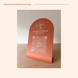 May include: A modern, orange-colored business sign with a white floral design and the text "Beautiful Things by Brooke". A white QR code is printed below the text, with an Instagram logo in the center.