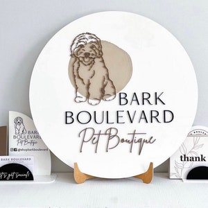 May include: A white, round sign with the text "BARK BOULEVARD Pet Boutique" and a dog illustration. Additional signage includes a QR code, social media handles, and "thank you" cards. The sign is displayed on a wooden stand.