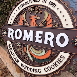 May include: A layered wooden sign with the name "ROMERO" in white block letters. The sign features a phoenix design in orange, green, and brown, with the text "ESTABLISHED IN 1981" and "MEXICAN WEDDING COOKIES".