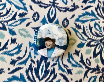 May include: A blue and white button featuring a photo of a person wearing a blue and white hat and a blue shirt with white polka dots.