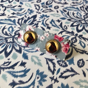 May include: A pair of silver stud earrings with a black and red image inside a clear glass dome.